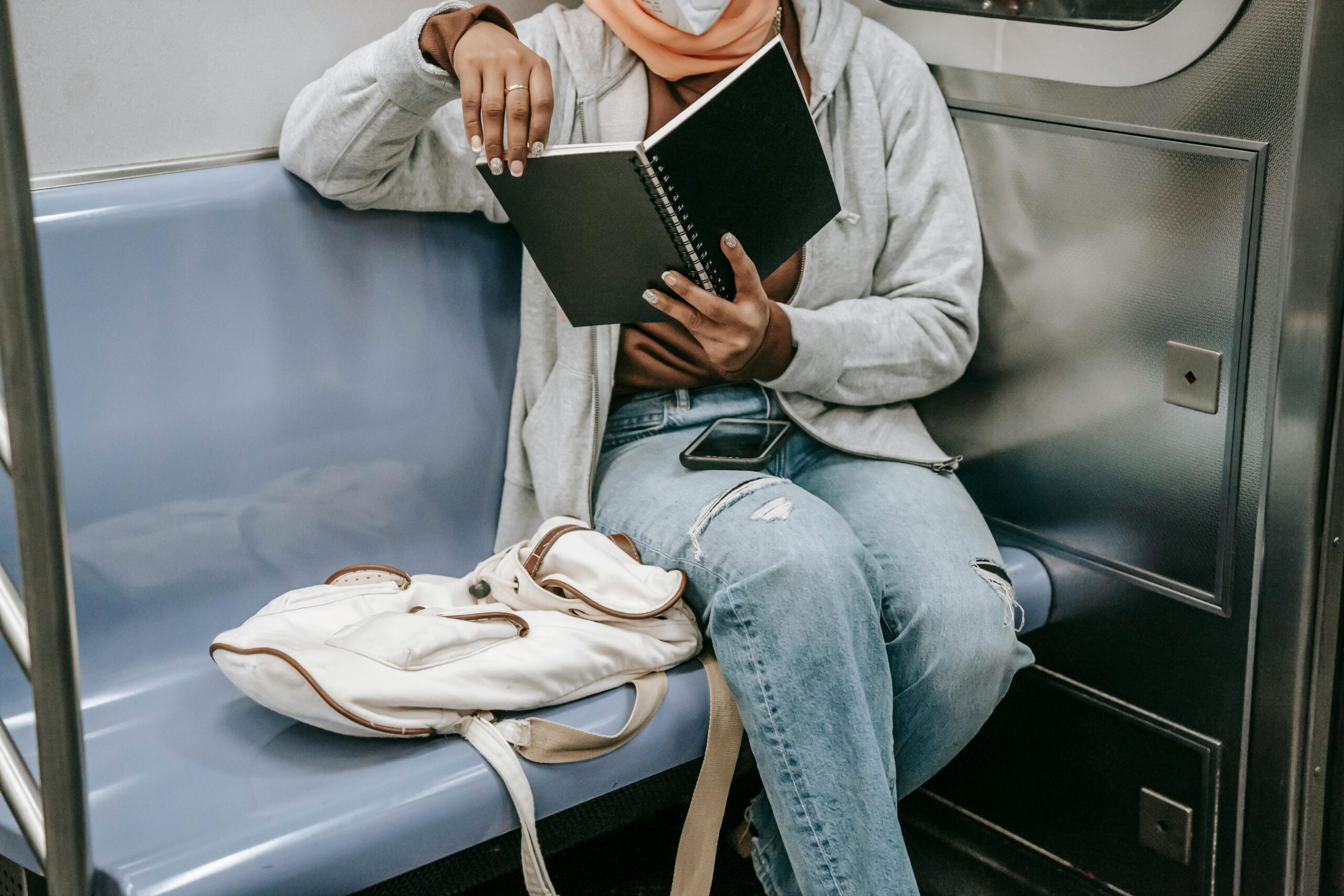 A person reading a book on a subway seat.
